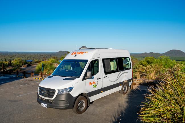 White Britz Mercedes campervan parked at a lookout with mountains in the background.