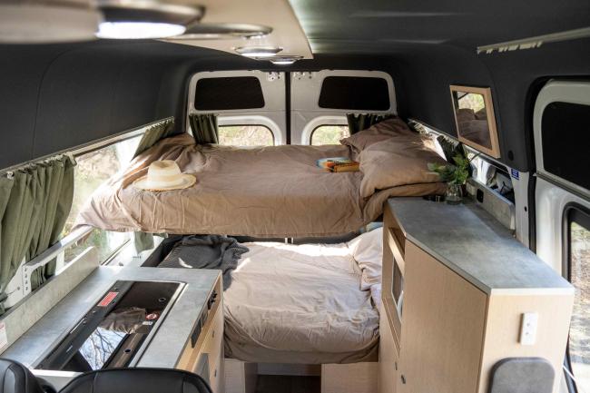 Campervan interior featuring stacked bunk beds, a grey kitchen counter, and light timber cabinetry.