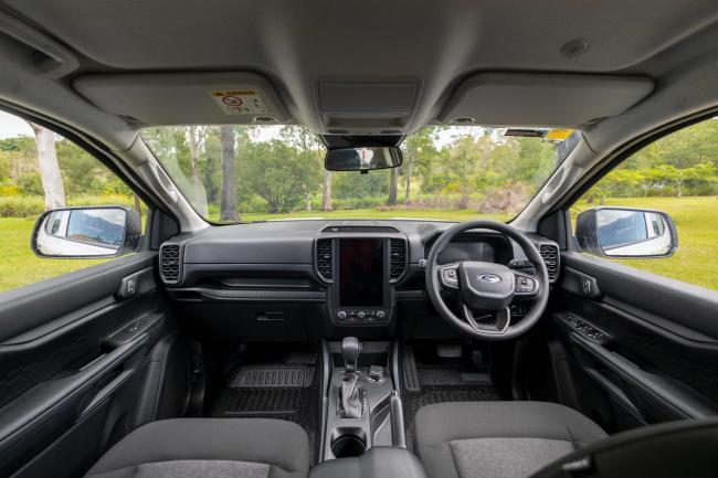 Right-hand drive modern Ford vehicle cabin interior with a central touchscreen, steering wheel, and grey fabric seats.