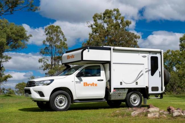 White Britz 4WD campervan parked on grass under a blue sky with scattered clouds.