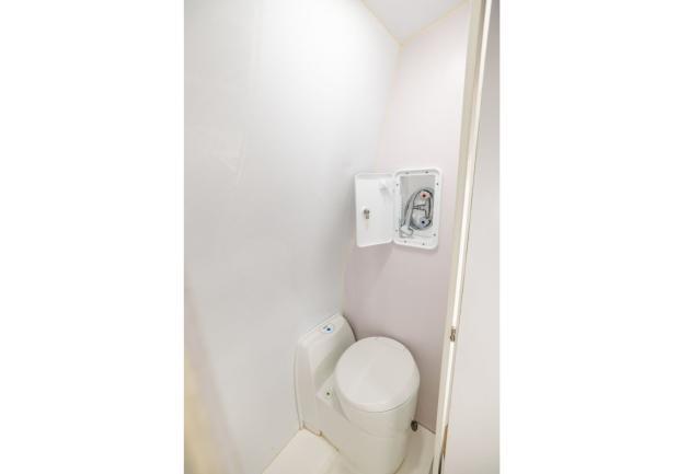 Compact campervan bathroom featuring a white cassette toilet and an open recessed wall shower unit.