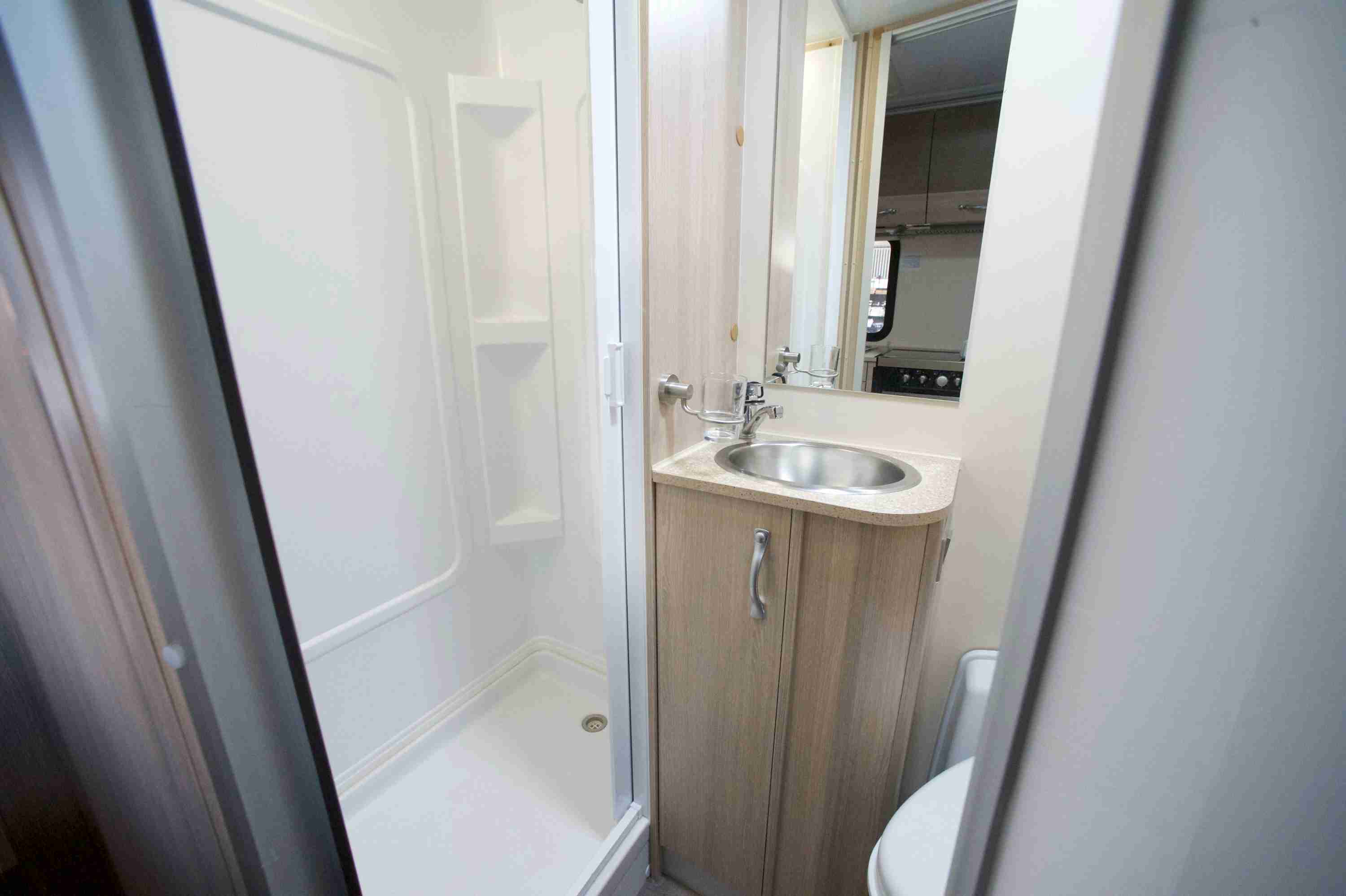 Compact campervan bathroom with a white shower cubicle, light timber-look vanity, stainless steel sink, and toilet.