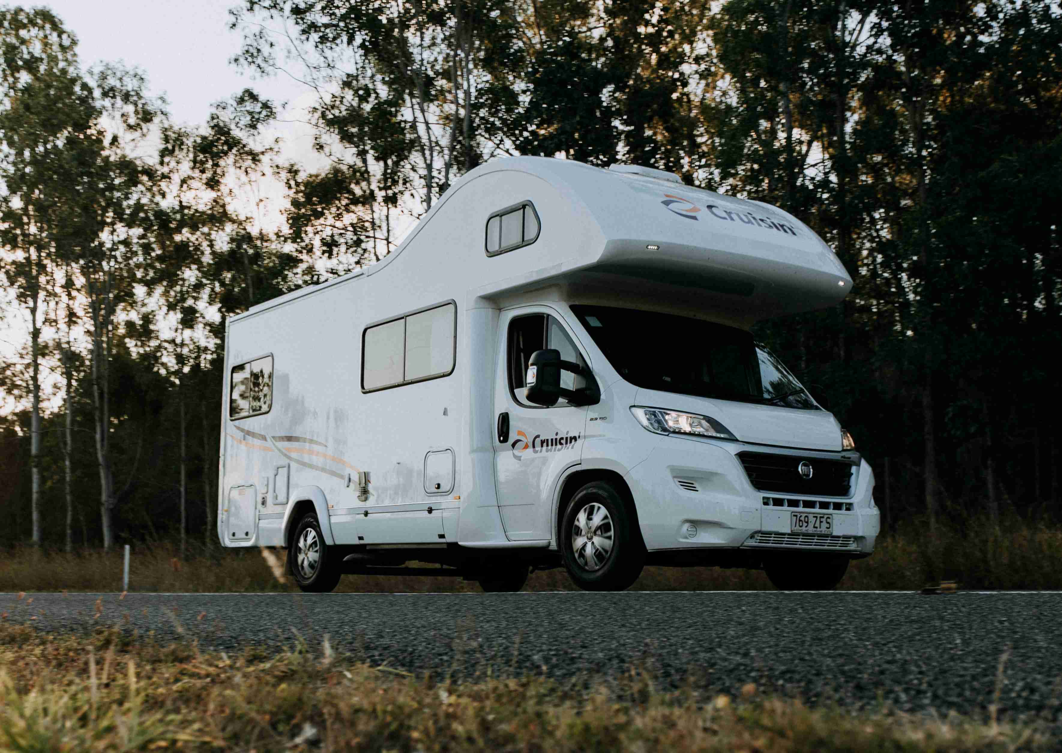 White Cruisin' campervan parked on an asphalt road with dense trees in the background.