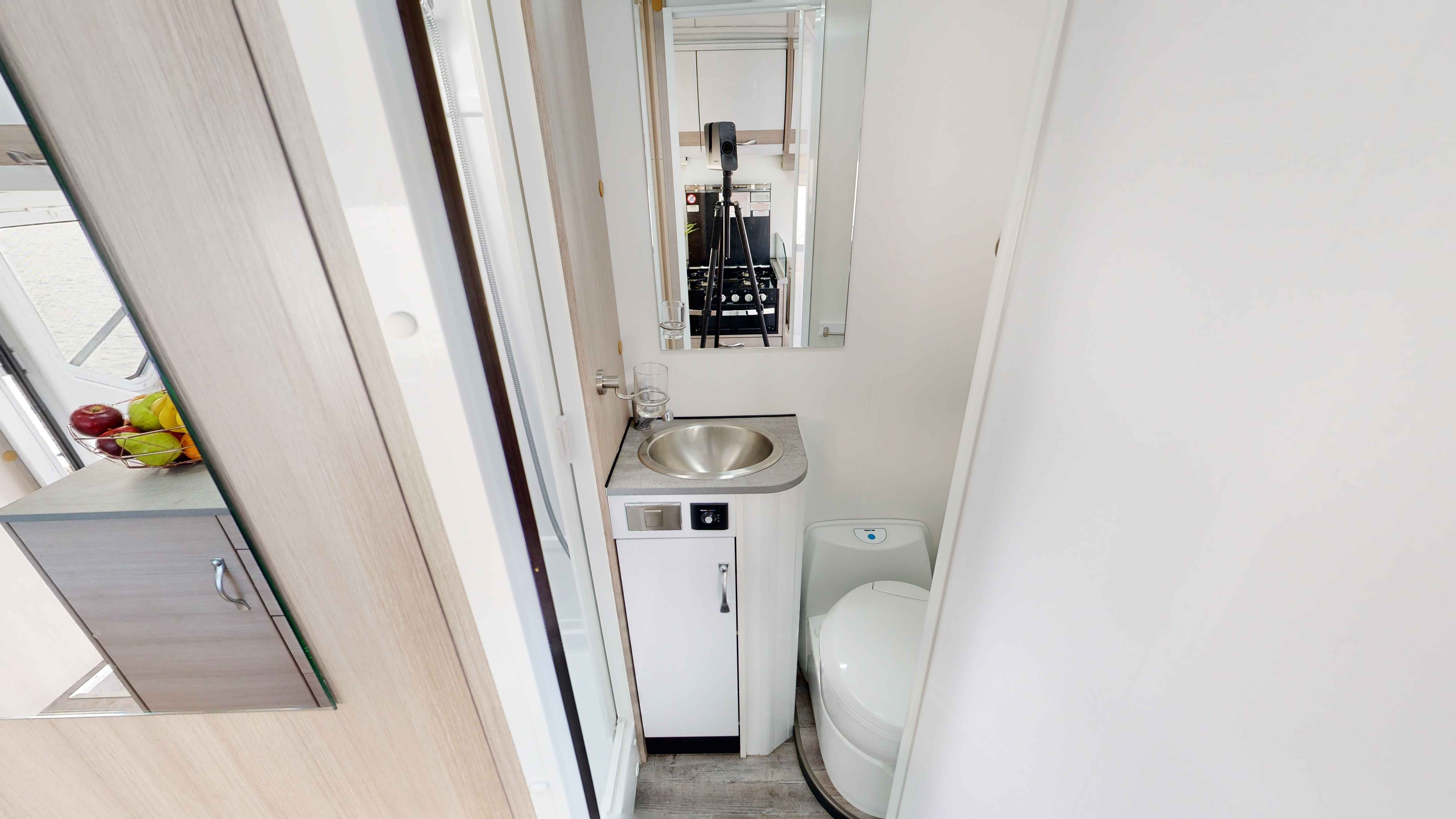 Compact campervan bathroom featuring a small stainless steel sink, white vanity, toilet, and wall mirror.