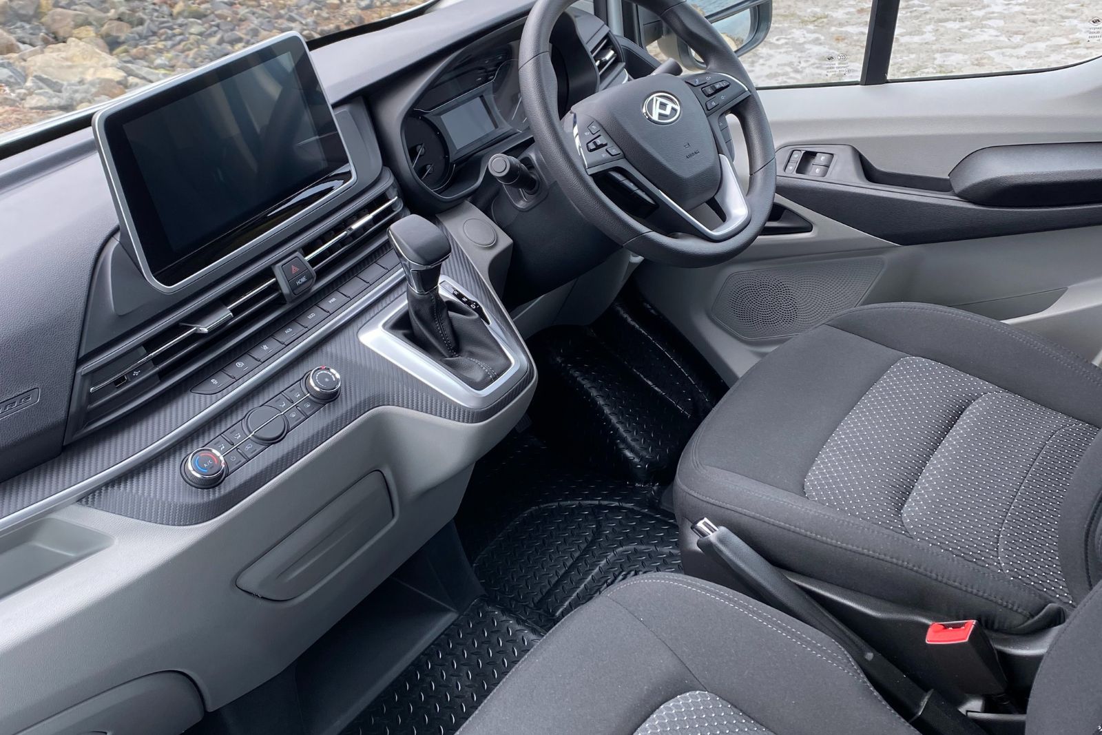Right-hand drive campervan cab with grey fabric seats, steering wheel, infotainment screen, and gear selector.