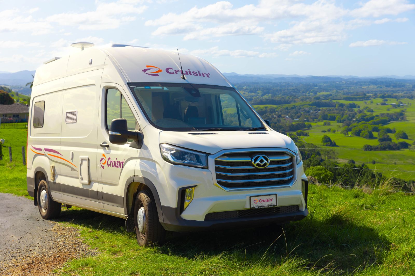 White Cruisin' campervan parked on a grassy hill overlooking a vast green valley.