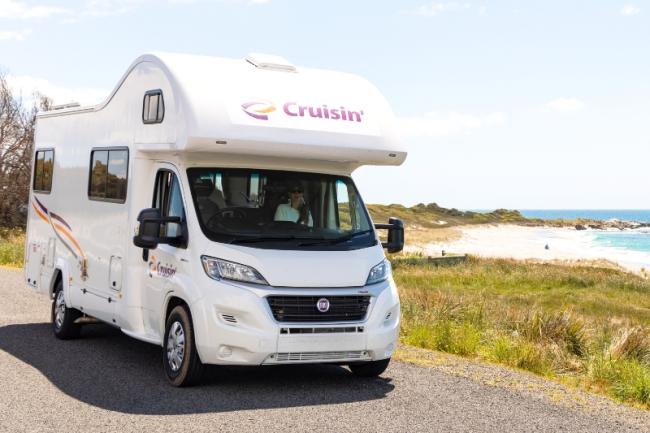 White Cruisin' campervan parked on a coastal road with a sandy beach and ocean in the background.