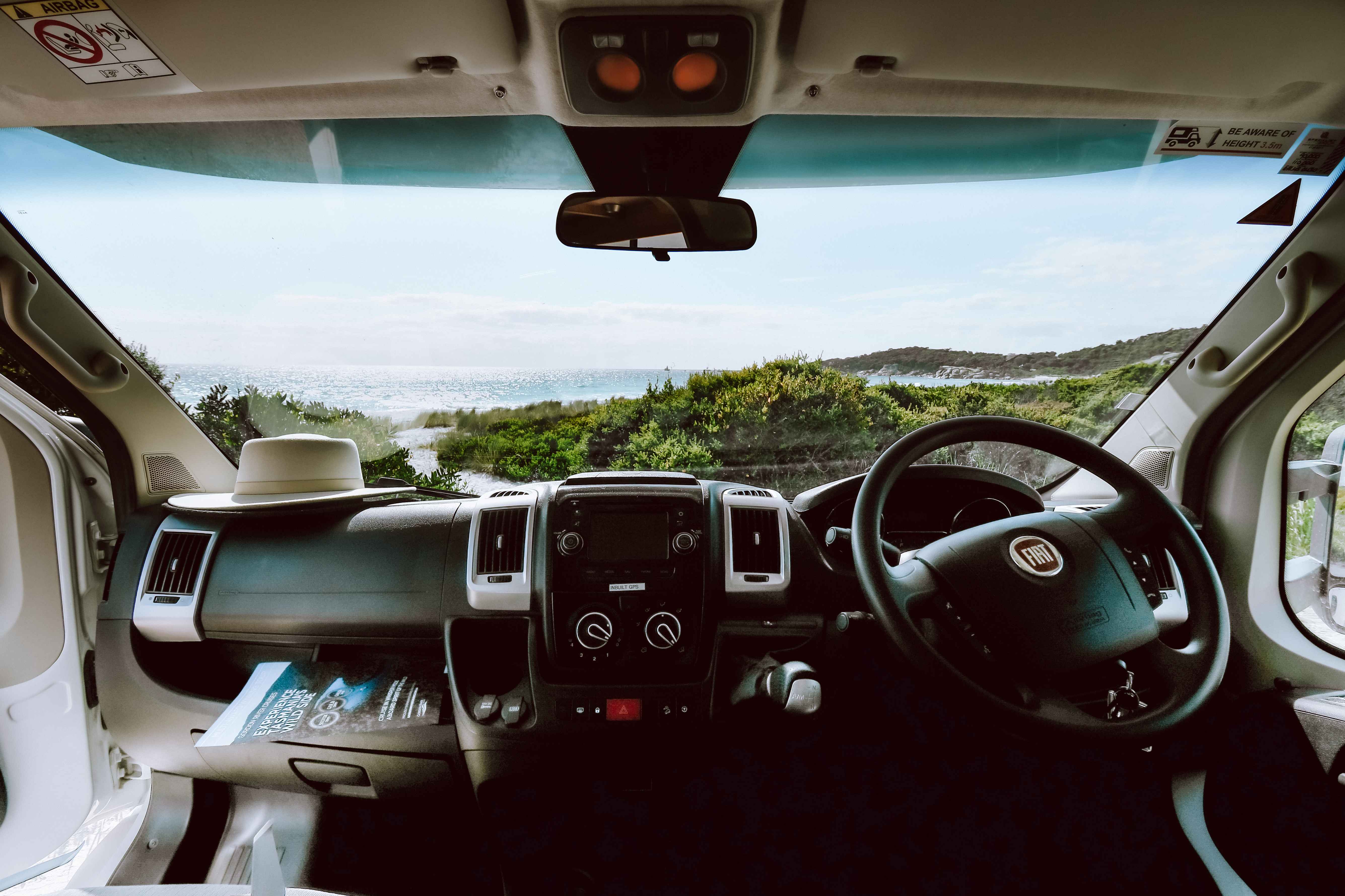 View from inside a Fiat campervan looking through the windscreen at a coastal beach and ocean.
