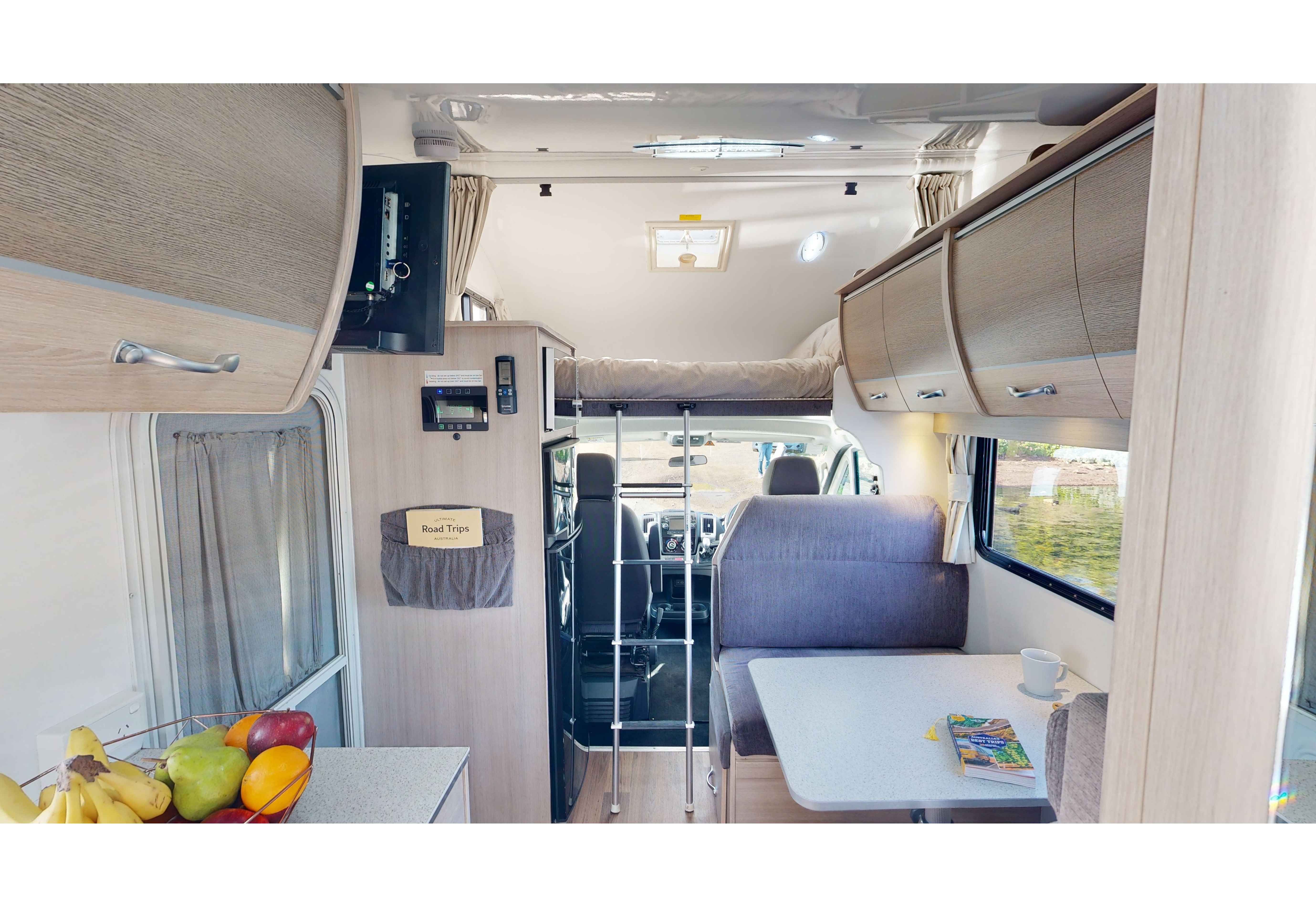 Campervan interior featuring a dining table, booth seating, a ladder to an over-cab bed, and overhead cabinets.