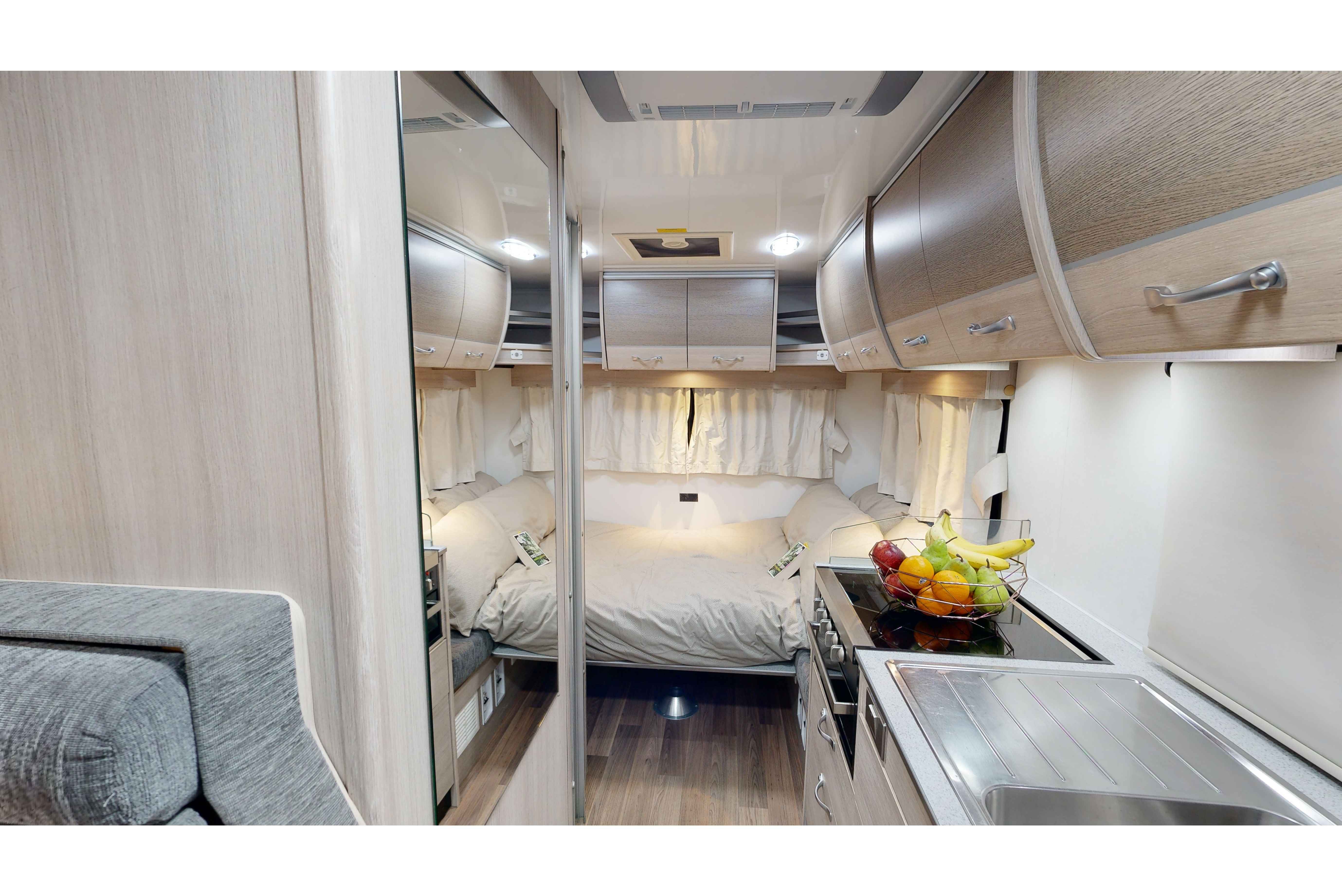 Compact campervan interior featuring a rear double bed, kitchen sink and stove, and overhead timber cabinets.