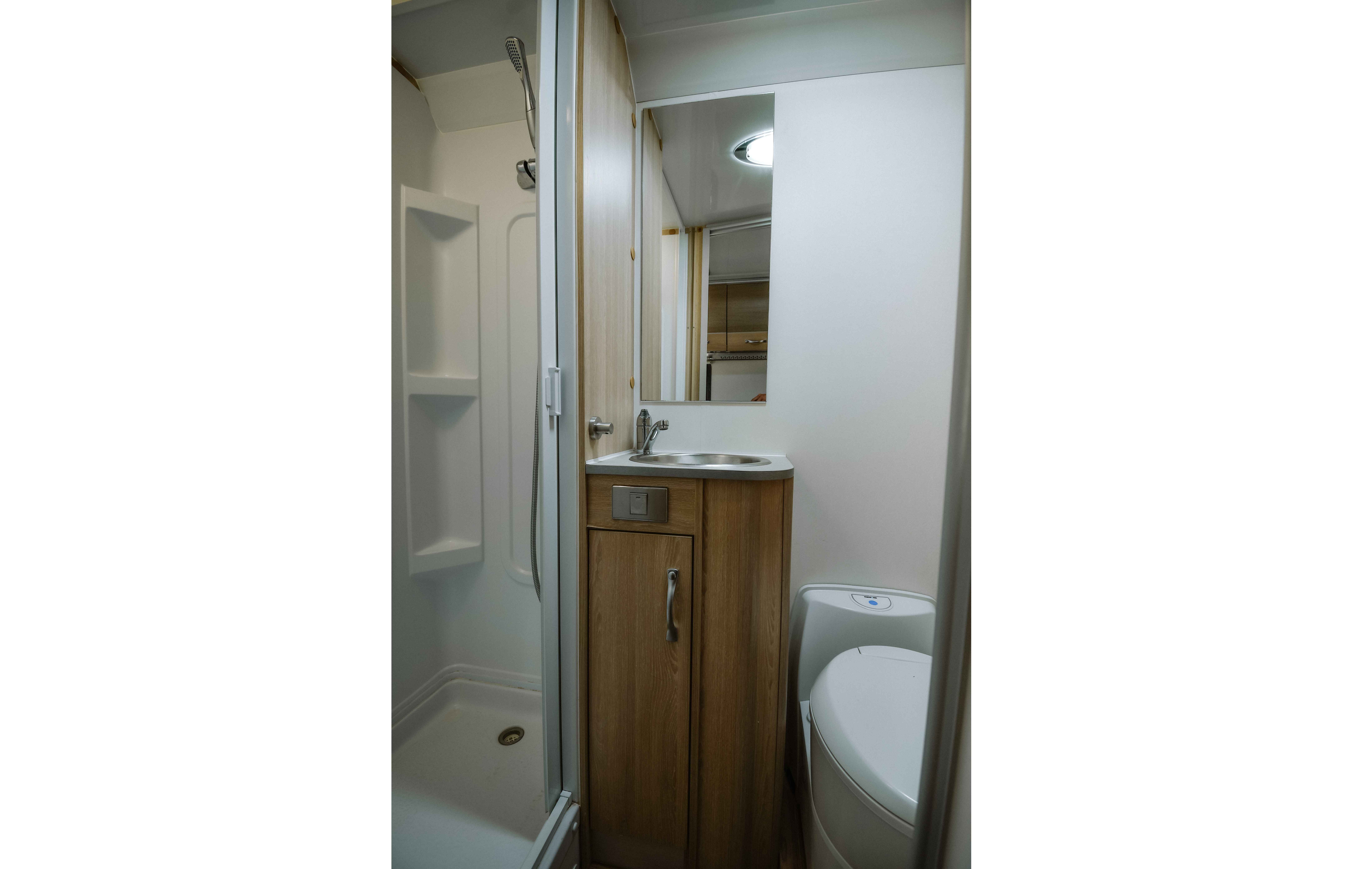 Compact campervan bathroom featuring a white shower cubicle, a timber vanity with a sink, and a cassette toilet.