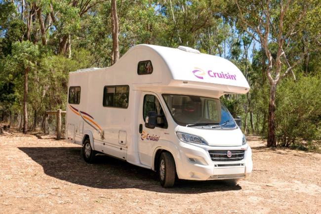 White Cruisin' campervan parked in a dirt clearing surrounded by trees.