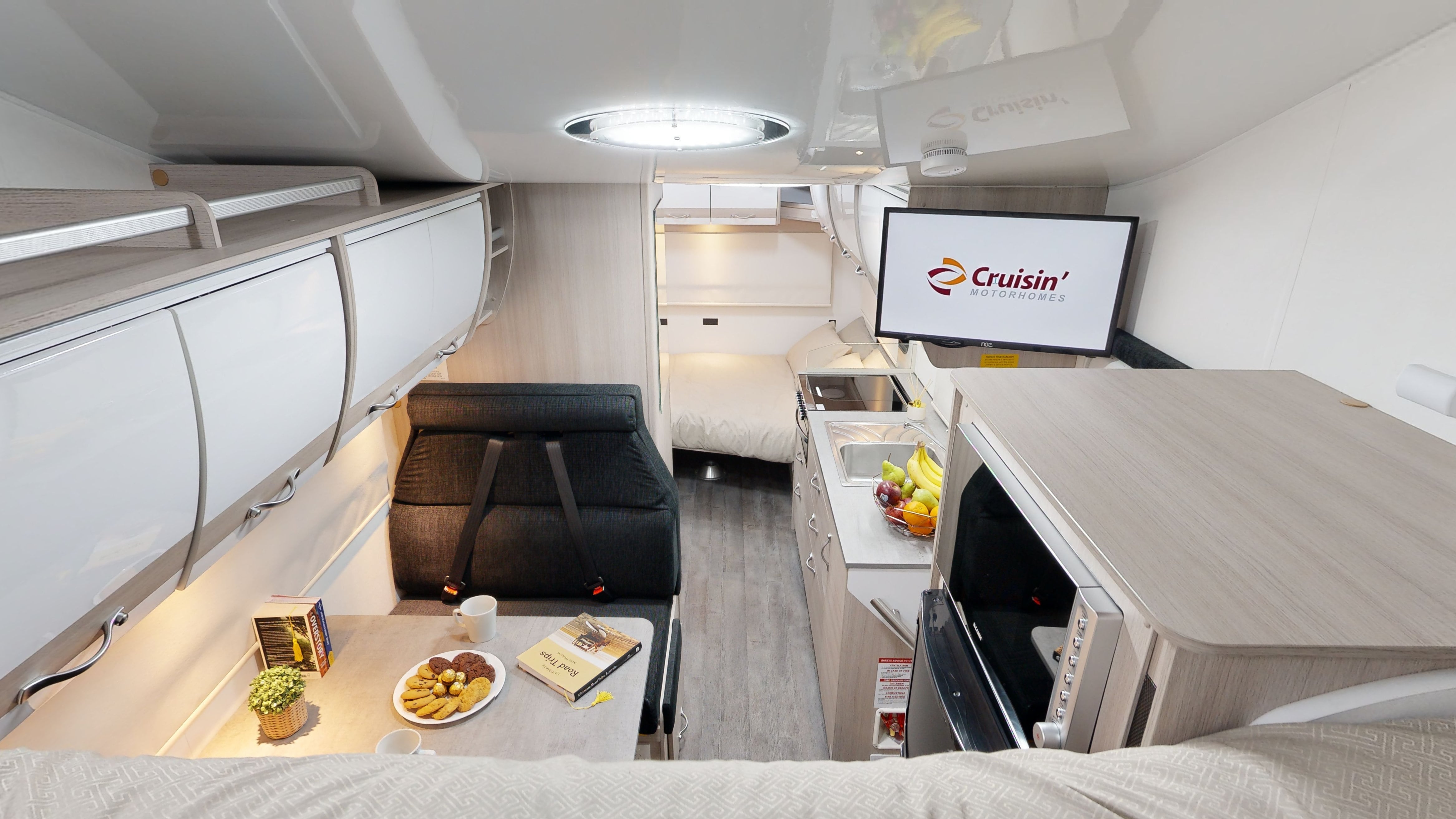 Inside a modern campervan looking down the aisle past a dining booth and kitchenette towards a rear bed.
