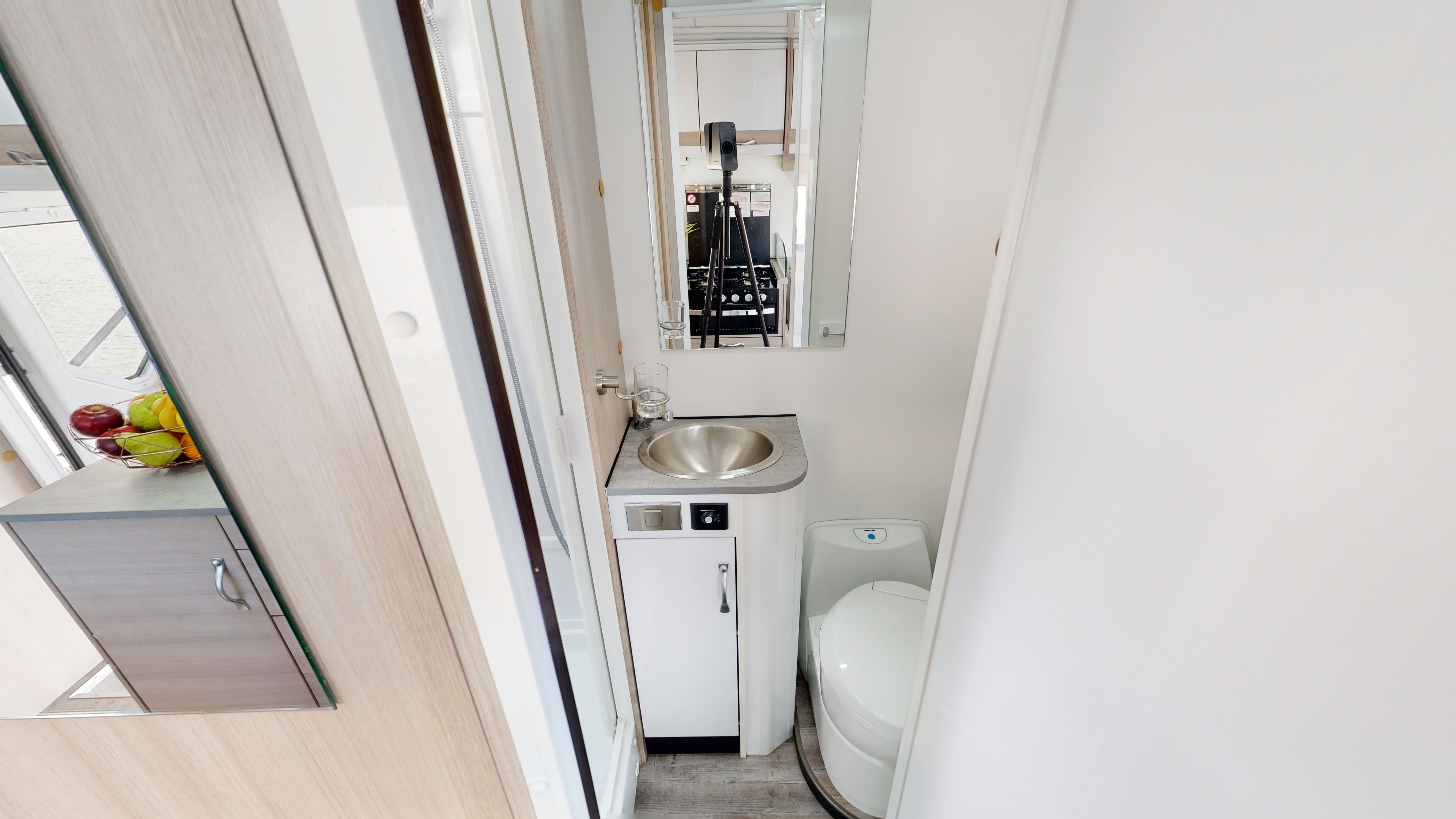 Compact campervan bathroom featuring a stainless steel basin, white vanity, mirror, and toilet.