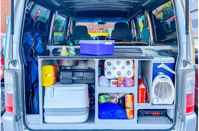 Organised campervan boot storage filled with a portable toilet, heater, cooler, and camping gear.