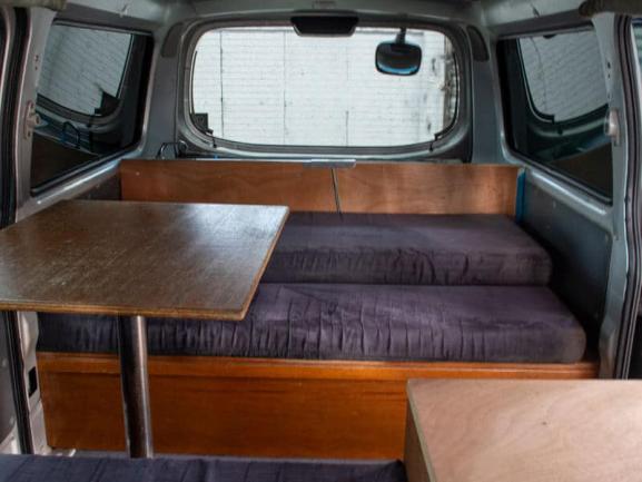 Campervan interior featuring dark cushioned bench seats and a timber table on a metal leg.