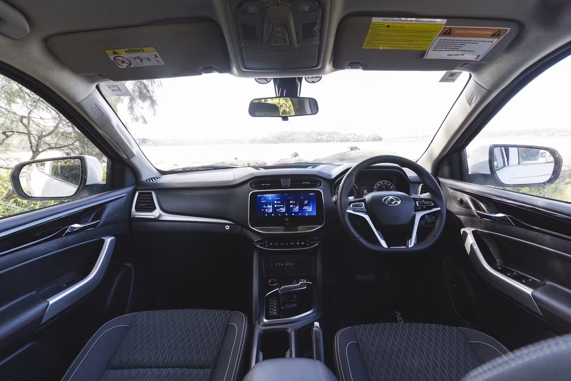 Right-hand drive campervan interior showing a black dashboard, steering wheel, centre console, and fabric seats.
