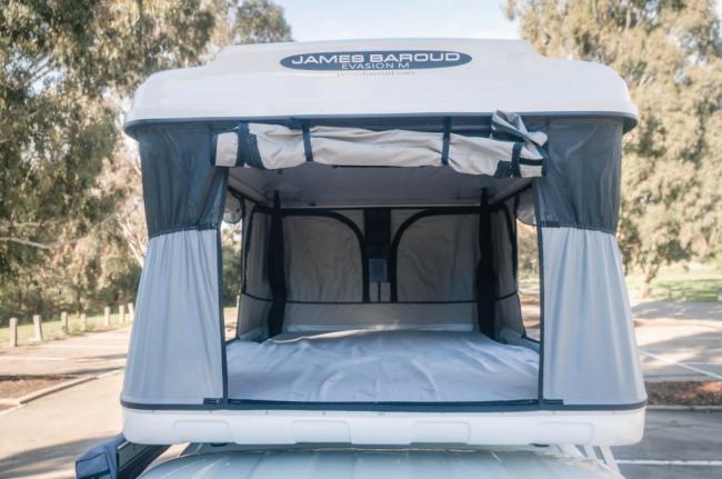 Open James Baroud Evasion M rooftop tent on a campervan, showing the grey fabric interior and mattress.