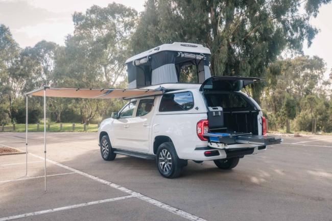 White dual-cab ute camper with a rooftop tent, extended side awning, and slide-out rear kitchen drawer system.