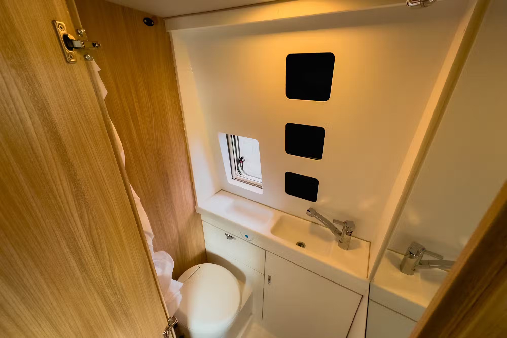 Compact campervan bathroom with a white toilet, integrated sink, and timber panelling.
