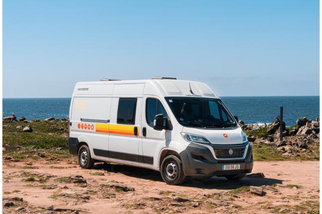 White campervan with retro orange stripes parked on a rocky coast overlooking the ocean.