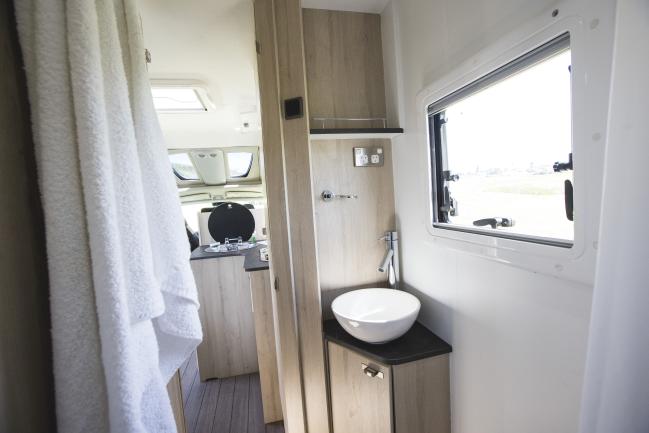 Compact campervan bathroom featuring a white vessel basin on a timber cabinet next to a window.