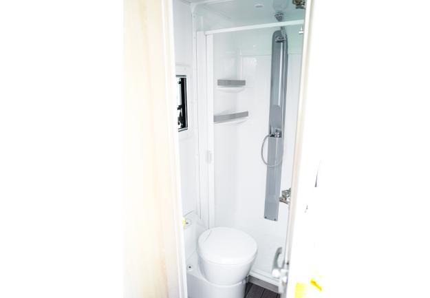 Compact campervan bathroom featuring a white toilet and integrated shower cubicle with grey fittings.