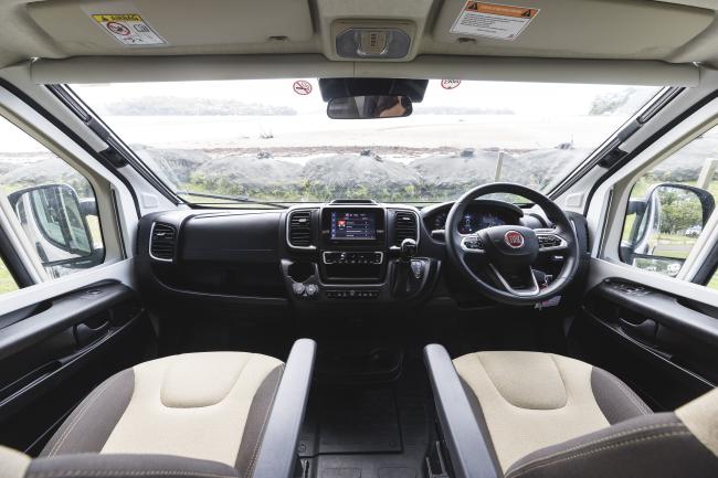 Modern campervan cabin interior featuring a right-hand drive dashboard, steering wheel, and beige fabric seats.