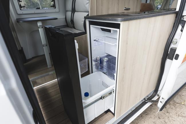 Open slide-out drawer refrigerator with drinks inside a compact campervan kitchen cabinet.