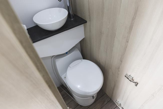 Compact campervan bathroom with a small round white basin on a dark benchtop above a white cassette toilet.