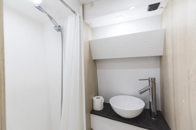 Compact campervan bathroom with a white shower cubicle beside a vanity with a white bowl basin and tall chrome tap.