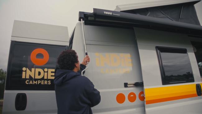 Person using a crank handle to extend a Thule awning on a grey Indie Campers campervan.