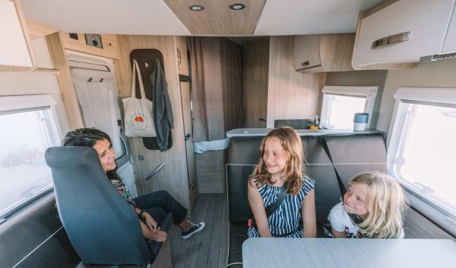 Woman and two young girls chatting inside the seating area of a modern campervan.