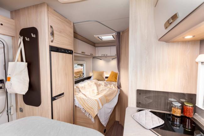 Interior of a campervan featuring light timber cabinets, a bed with a yellow blanket, and a kitchen cooktop.