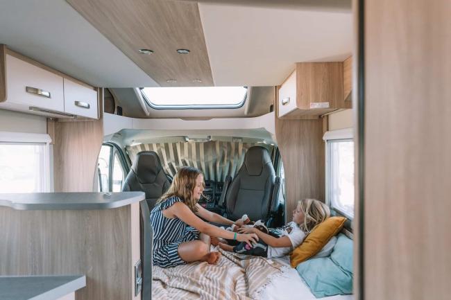 Two children play on a bed inside a campervan interior with cabin seats in the background.