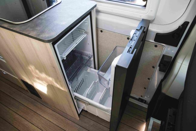 Open drawer fridge in a campervan kitchen unit with light-coloured cabinetry and dark benchtop.