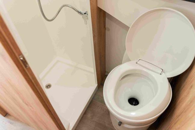 Compact campervan bathroom with a small shower cubicle on the left and a white toilet with its lid open on the right.