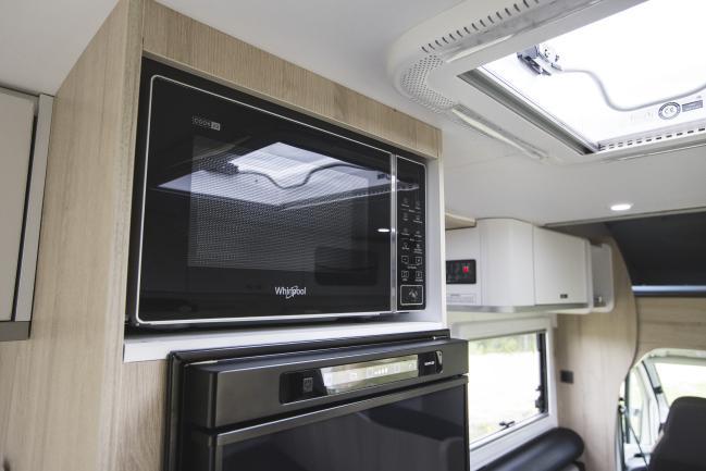 Black Whirlpool microwave built into timber-look cabinetry above a fridge inside a campervan.