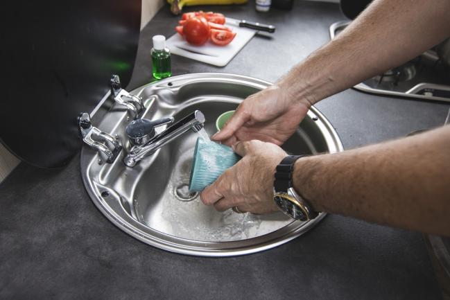 Hands washing a turquoise cup under a running tap in a compact campervan sink.