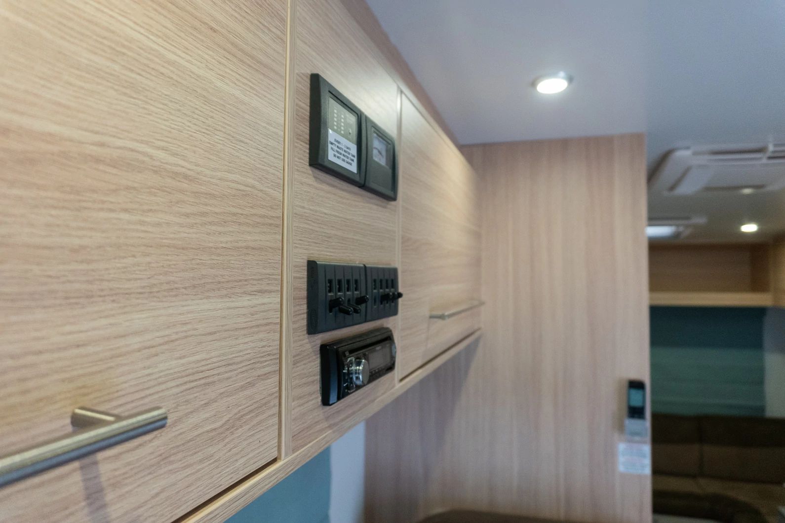 Control panel with switches, gauges, and stereo on light timber cabinets inside a campervan.