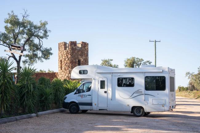 White Mighty campervan parked on a dirt road next to a stone tower.