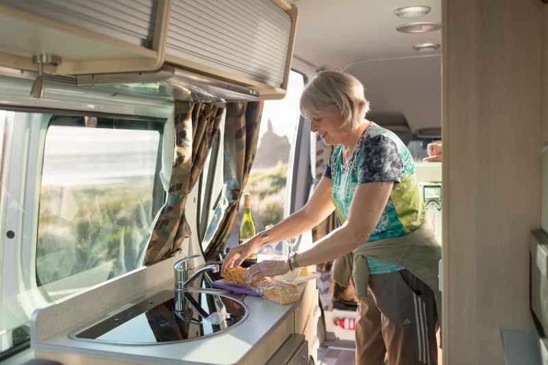 A woman prepares food on a kitchen counter inside a campervan.