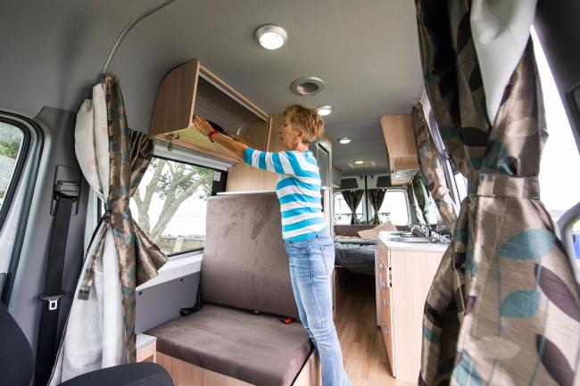 Woman in a striped top opening an overhead storage cabinet inside a campervan.