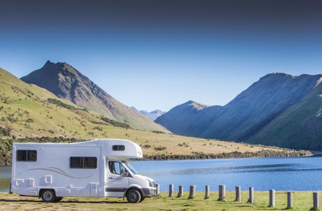White campervan parked on grass by a blue lake with steep green mountains in the background.