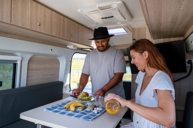 Couple preparing a meal and pouring juice at a table inside a campervan.