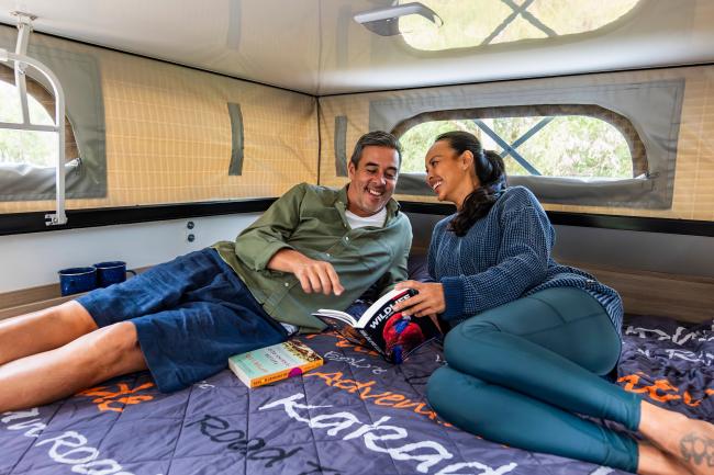 Man and woman smiling while reading a book together inside a campervan pop-top tent.