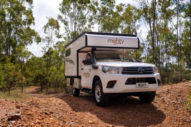 White Mighty 4WD campervan parked on a red dirt track in an Australian bush forest.