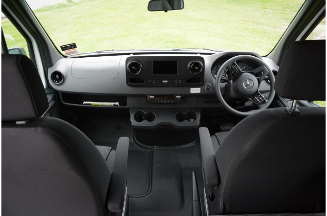 Cab interior of a right-hand drive Mercedes campervan with black seats, steering wheel, and centre console.