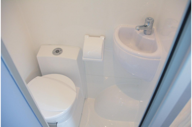 Compact white campervan bathroom with a cassette toilet, toilet roll holder, and a small corner basin.