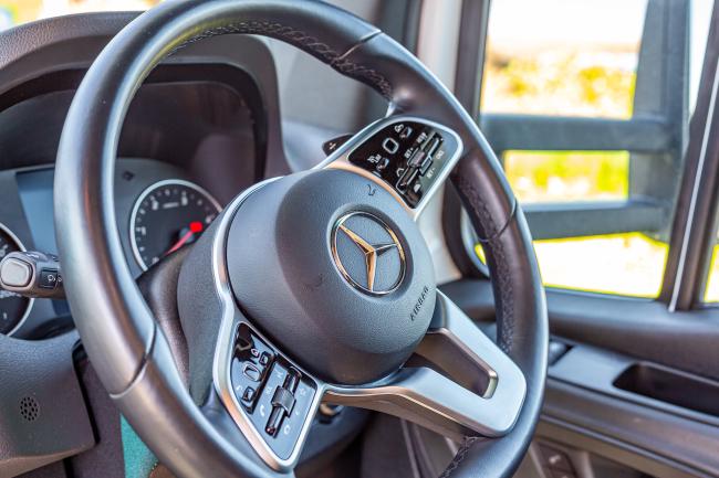 Mercedes-Benz steering wheel with integrated controls and central emblem inside a campervan cab.